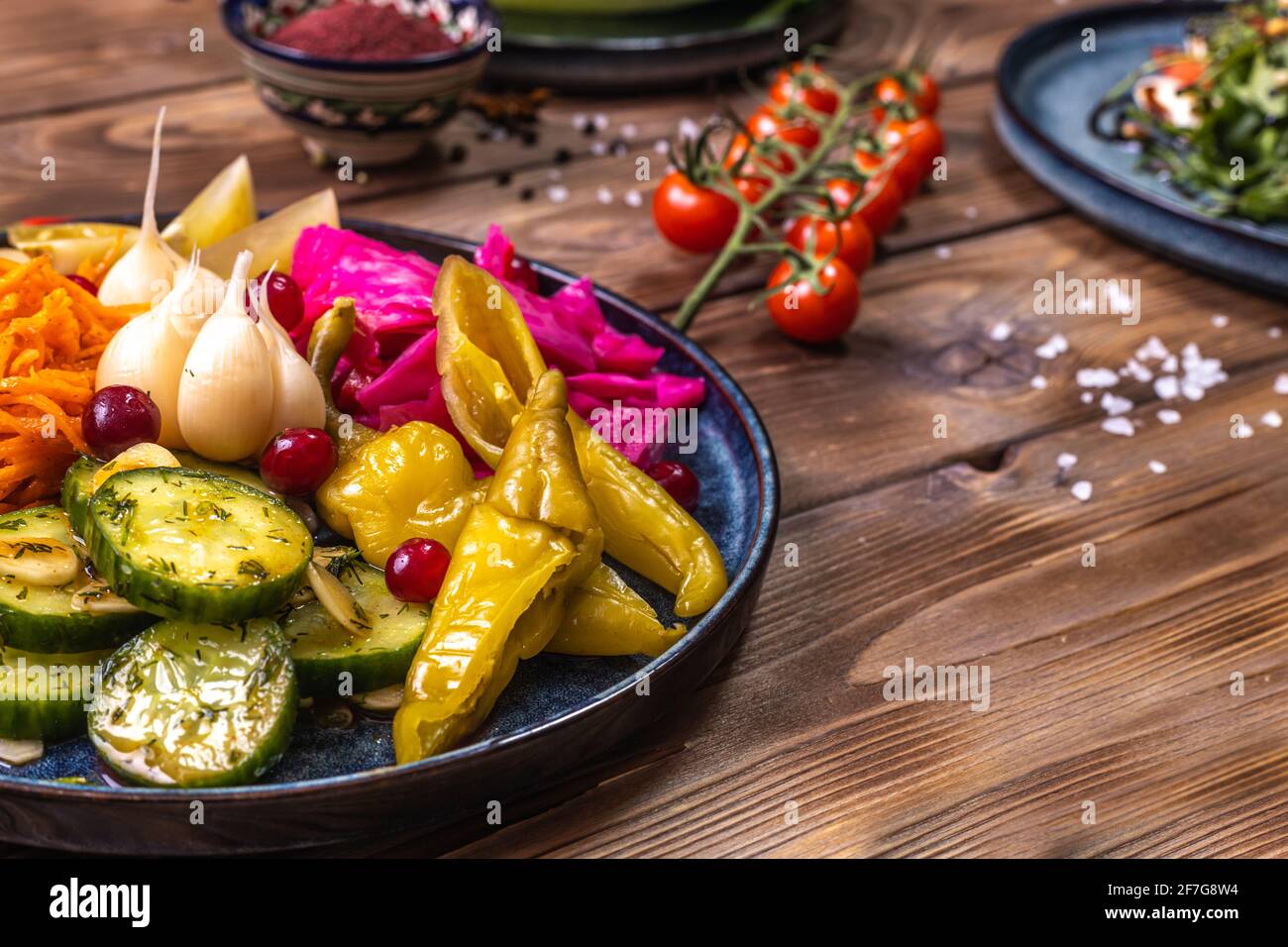 Verdure sottaceto: Peperoni, carote, aglio, cavolo giacciono su un piatto su sfondo ligneo decorato con peperoncino, rosmarino. Il concetto di lui Foto Stock