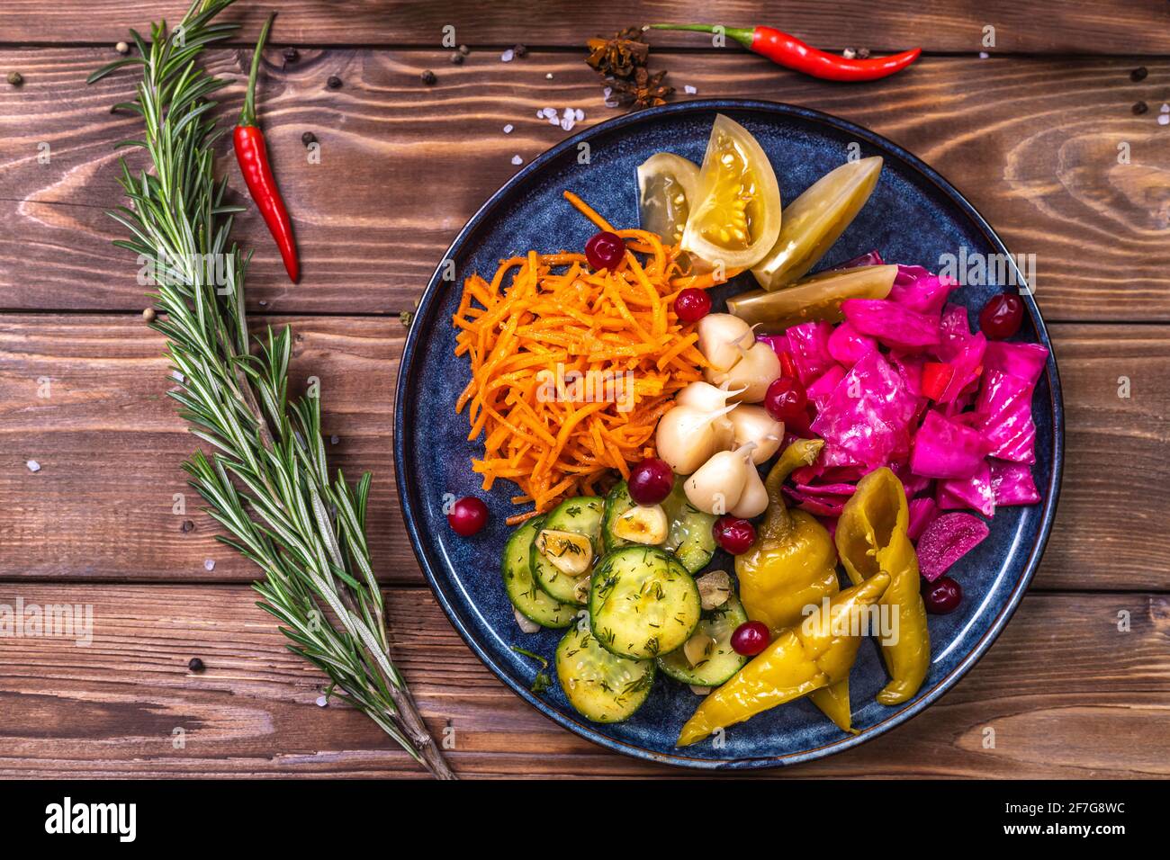 Verdure sottaceto: Peperoni, carote, aglio, cavolo giacciono su un piatto su sfondo ligneo decorato con peperoncino, rosmarino. Il concetto di lui Foto Stock