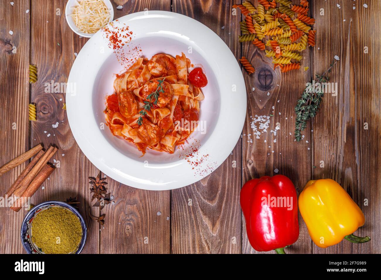 Pasta con salsa in un piatto, peperone, timo e altre spezie su fondo di legno marrone. Layout piatto. Foto Stock