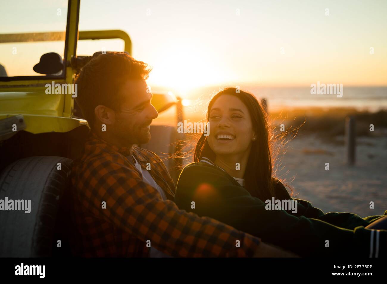 Felice coppia caucasica appoggiata contro la spiaggia buggy vicino al mare sorridente al tramonto Foto Stock