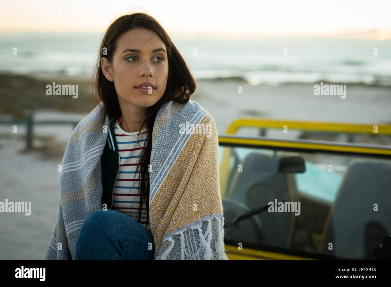 Donna caucasica felice seduta sulla spiaggia buggy vicino al mare indossare lo scialle guardando avanti Foto Stock