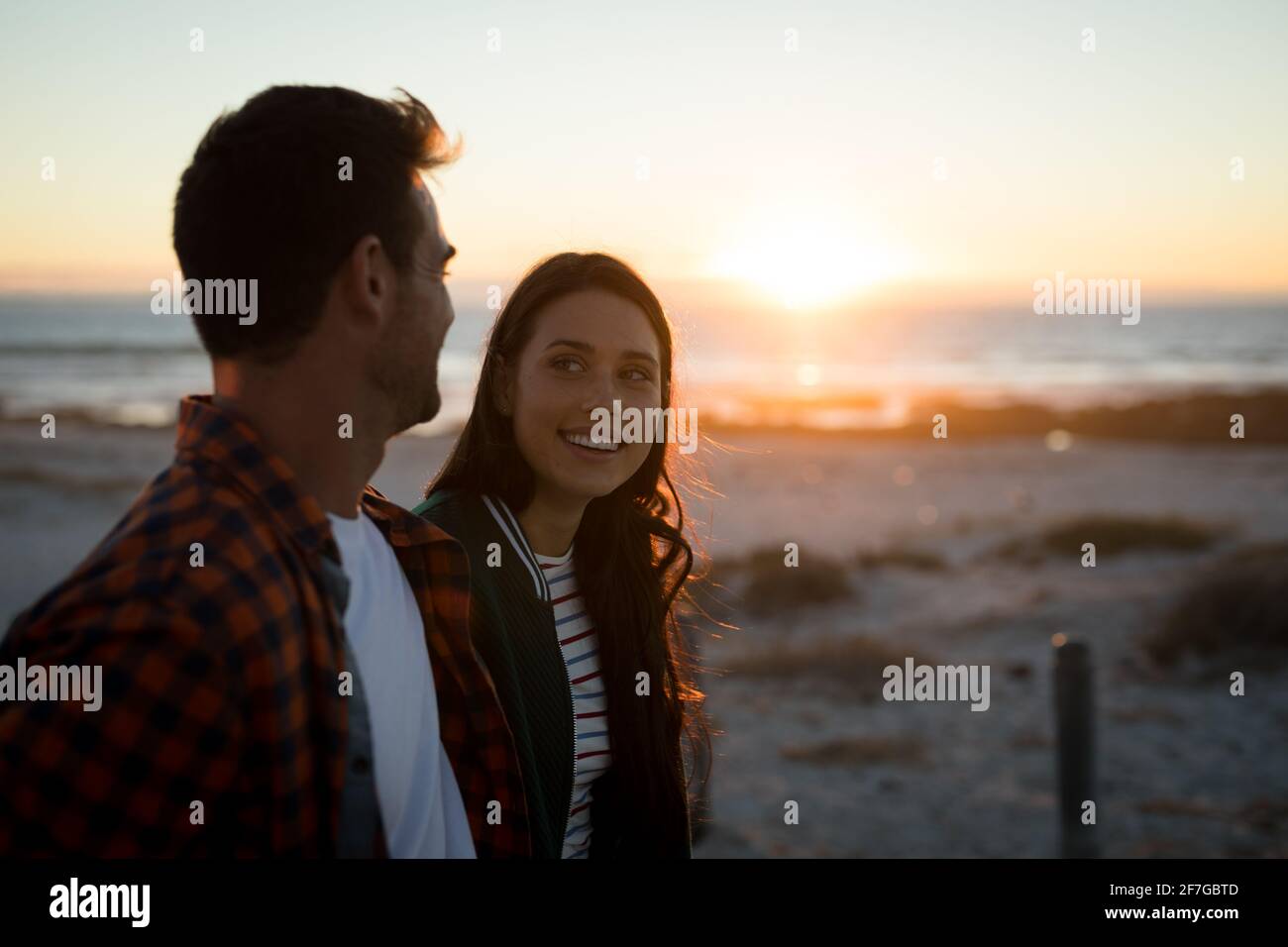 Felice coppia caucasica sulla spiaggia guardando l'un l'altro durante il tramonto Foto Stock