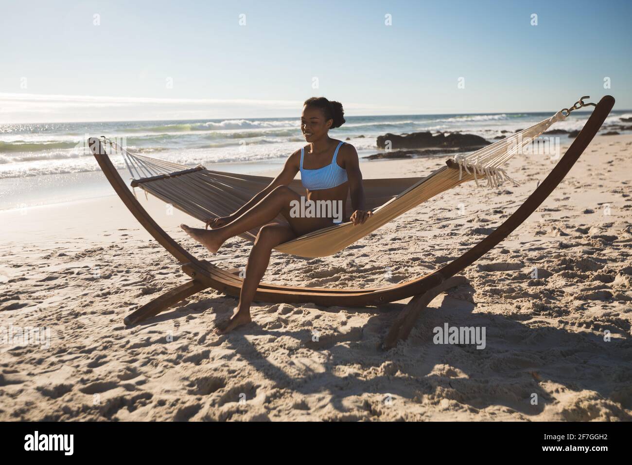 Donna afro-americana felice seduta in amaca sulla spiaggia Foto Stock