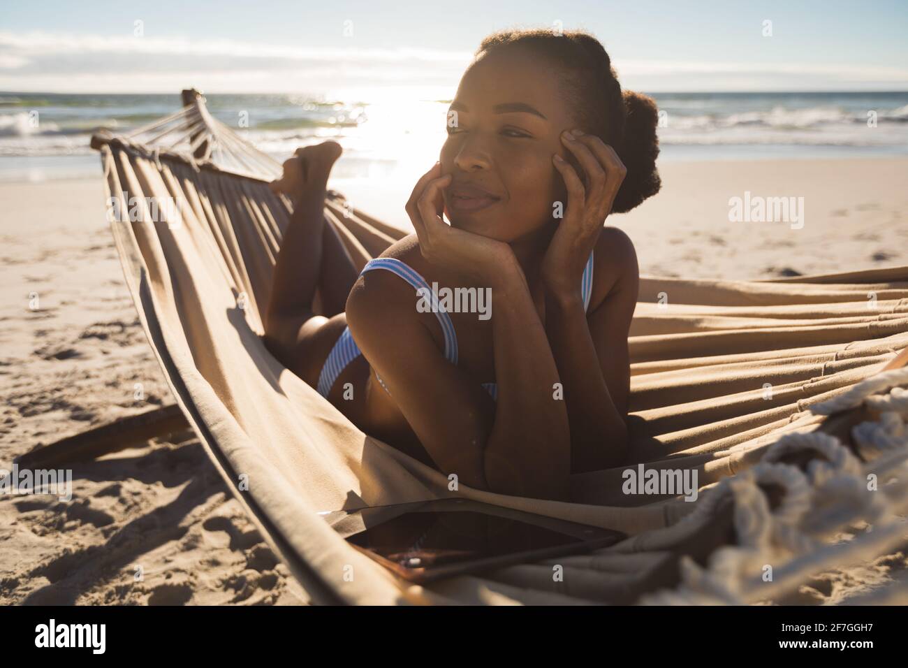 Donna afro-americana felice sdraiata in amaca sulla spiaggia guardando avanti Foto Stock