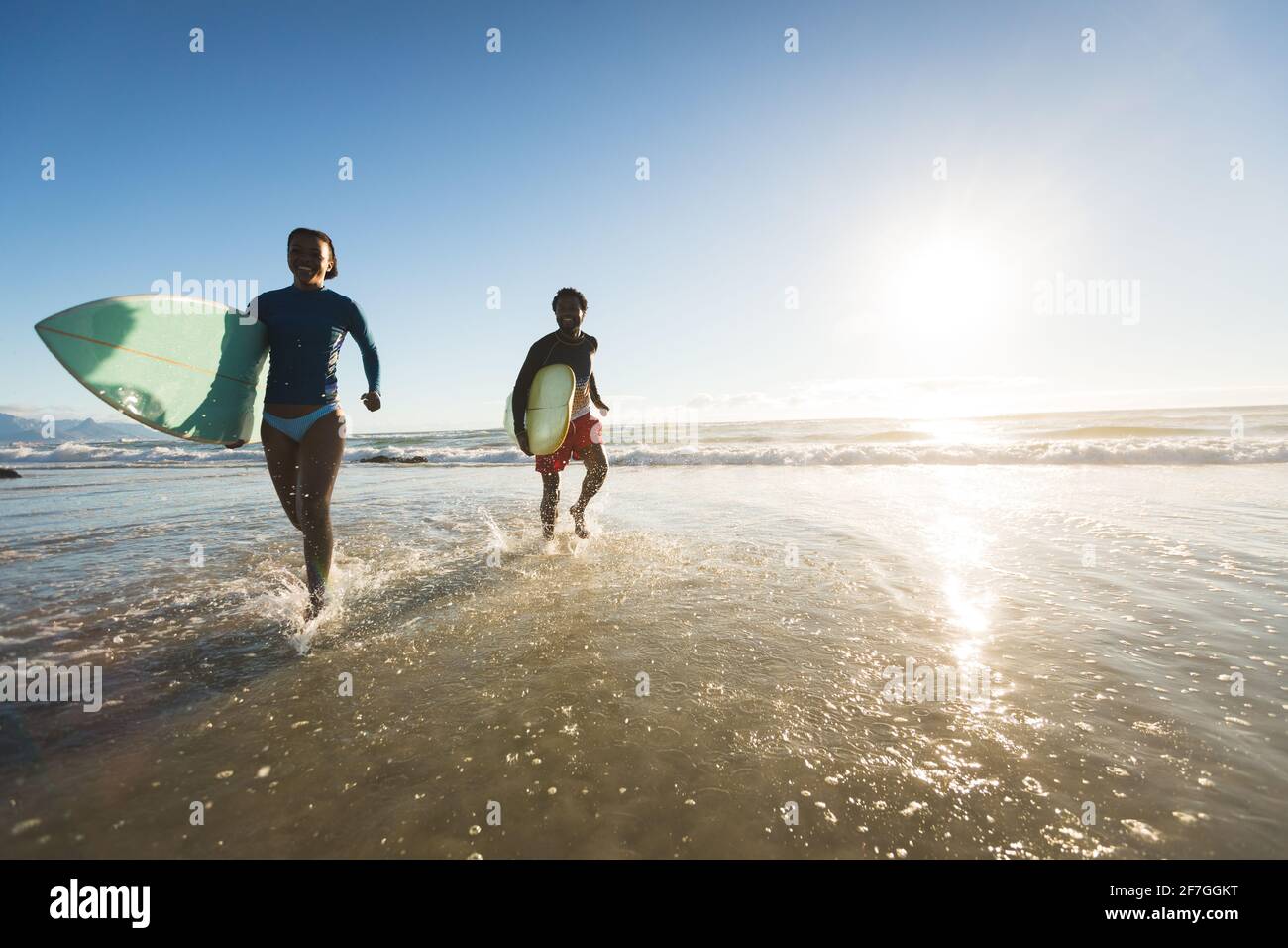 Felice coppia afroamericana che corre il mare portando tavole da surf Foto Stock