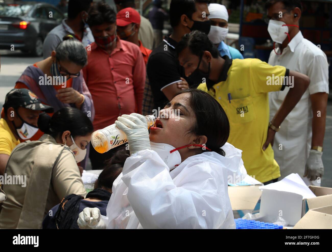 Un operatore sanitario stanco che dissetava durante il prelievo di campioni di tampone per il test di reazione a catena della polimerasi a trascrizione inversa (RT-PCR) Covid-19 in tempo reale sul lato della strada a Nuova Delhi. Foto Stock