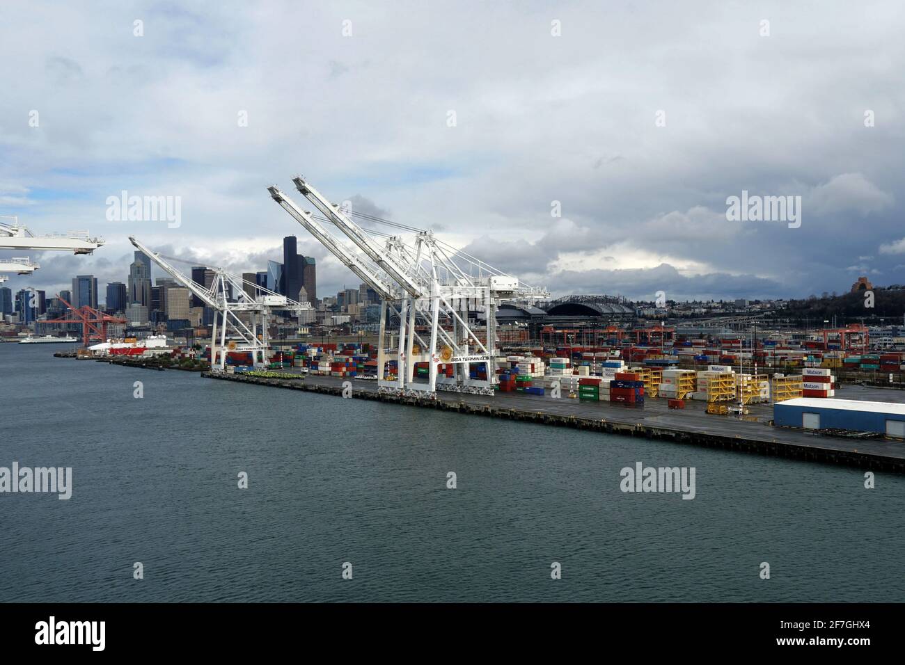 Terminal per container con gru a portale situato a Seattle, Washington, USA con profilo di grattacieli sullo sfondo sotto il suggestivo cielo coperto. Foto Stock