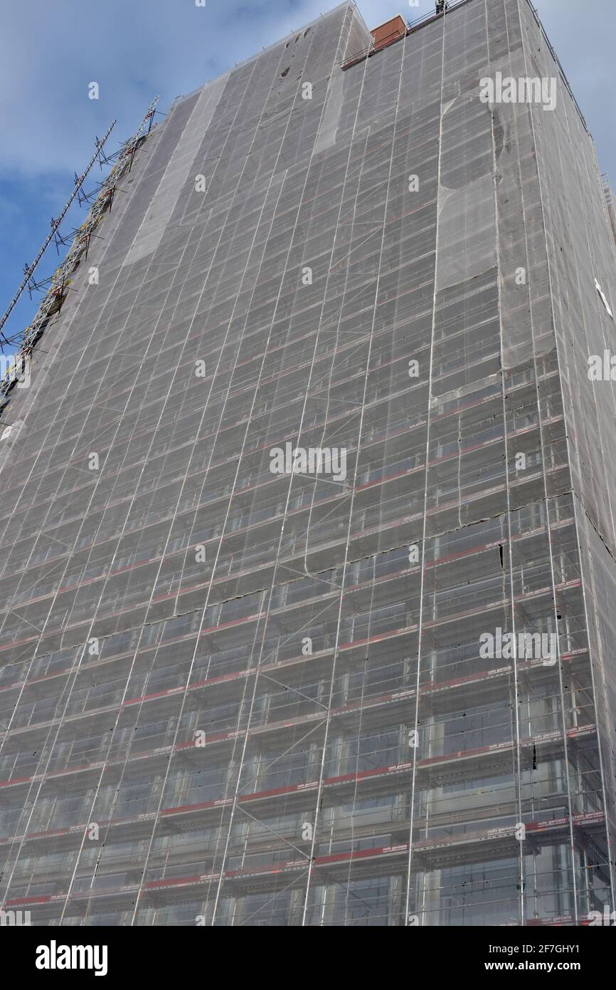 Alto edificio per uffici aziendali in citta' in costruzione con impalcature circondate da rete di sicurezza bianca o rete a maglia ad alta densità in polietilene. Foto Stock