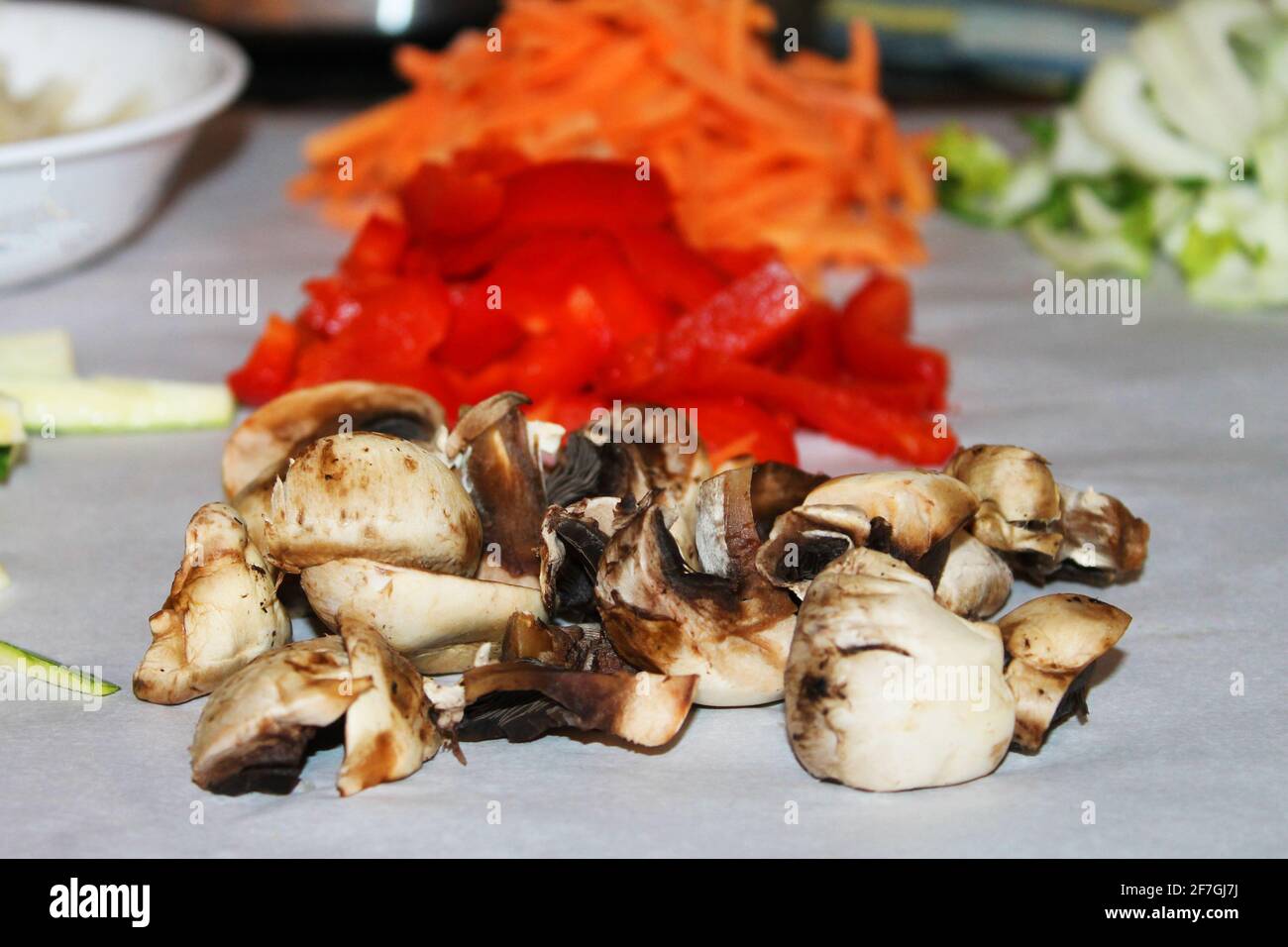 Primo piano di funghi tritati, pepe rosso, carote e altre verdure preparate per la preparazione dei pasti. La messa a fuoco è sui funghi in primo piano dell'immagine. Foto Stock