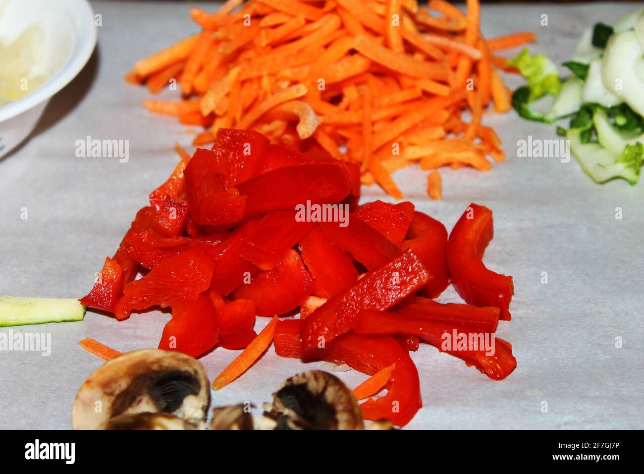 Primo piano di funghi tritati, pepe rosso, carote e altre verdure preparate per la preparazione dei pasti. La messa a fuoco è sui peperoni rossi al centro dell'immagine. Foto Stock