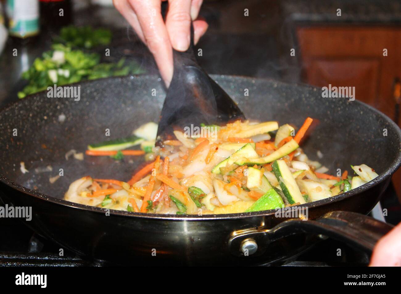 Un primo piano di una persona mescolare le verdure fritte. Vista parziale della mano sull'utensile e altra mano sull'impugnatura della padella. Foto Stock