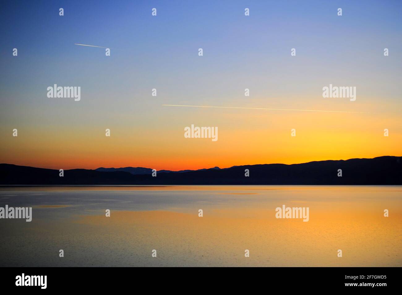 Tramonto in lontananza sopra la superficie con acqua. Le montagne si possono vedere all'orizzonte. Foto Stock