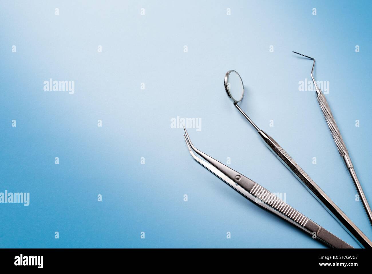 Strumenti dentistici: Specchio, sonda dentale e pinzette giacenti a destra su sfondo blu a gradiente. Foto Stock