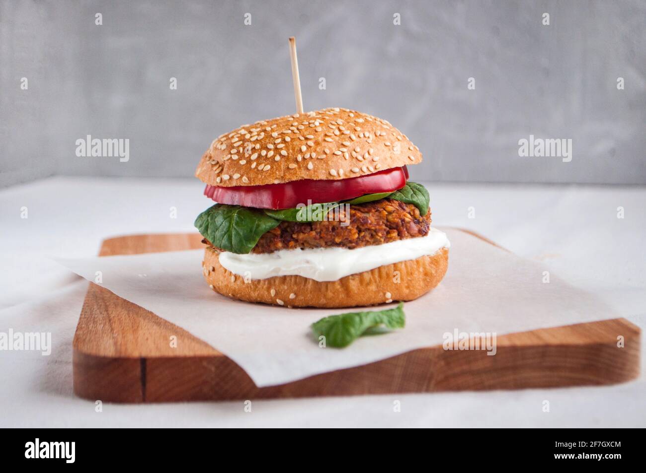 Hamburger vegano con fagioli rossi, pepe rosso, spinaci, yogurt bianco e foglie di insalata fresca e verdure tagliate sullo sfondo. Foto Stock