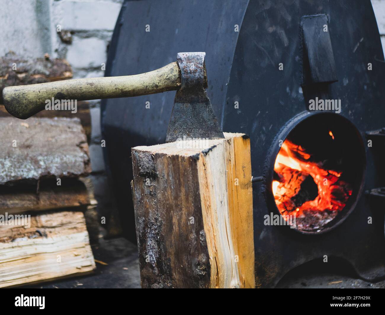 Vecchio ascia, legna da ardere e stufa a legna con fiamma del fuoco. Illuminazione della stufa Foto Stock