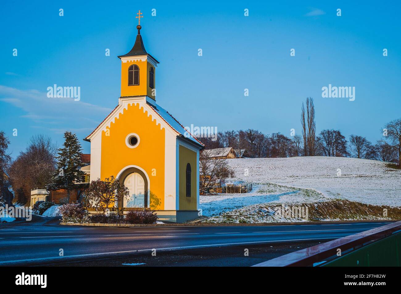 Una piccola chiesa gialla o un capel in Austria in un periodo invernale soleggiato. Tipica cappella in Austria o parte centrale d'europa illuminata dal sole serale d'autunno. Som Foto Stock