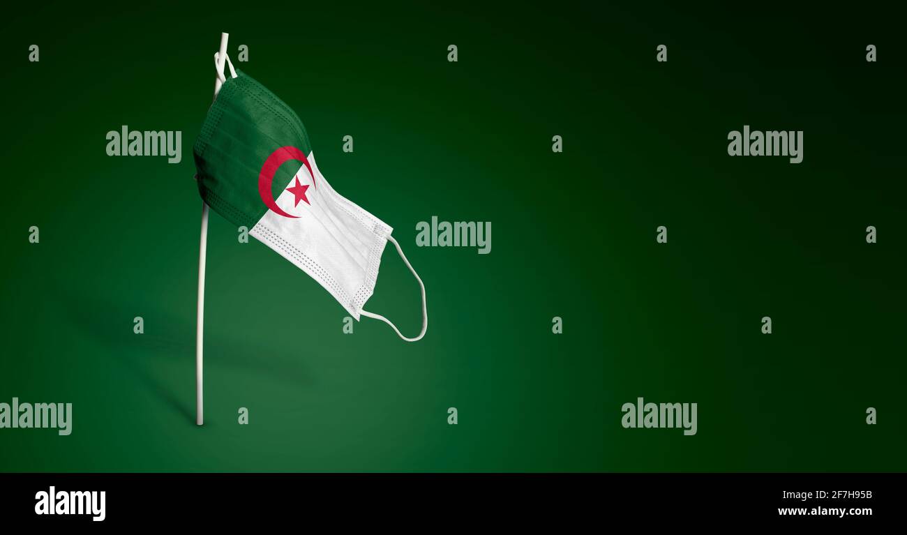 Maschera algerina su sfondo blu scuro. Bandiera ondulata dell'Algeria dipinta su maschera medica sul palo. Flag di attacco del virus. Concetto del banner della Fight ag Foto Stock