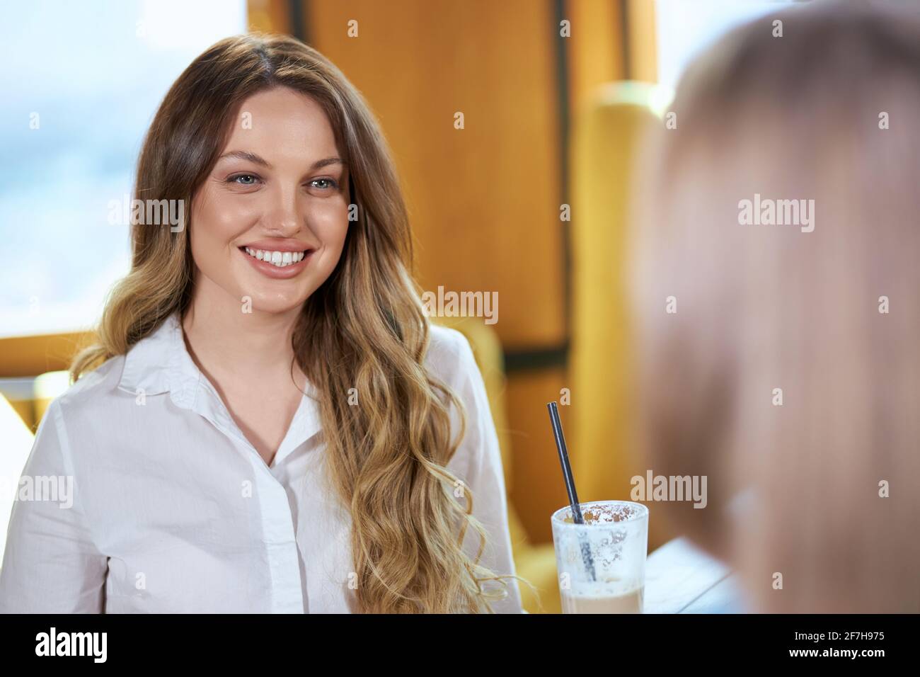 Primo piano ritratto di sorridente bella donna con bei capelli lunghi bere caffè e parlare con la ragazza in caffetteria. Concetto di comunicazione con buon umore. Foto Stock