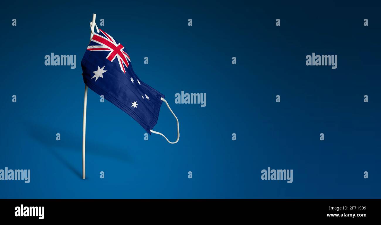 Maschera australiana su sfondo blu scuro. Bandiera ondulata dell'Australia dipinta su maschera medica sul palo. Flag di attacco del virus. Concetto della bandiera della coscia Foto Stock