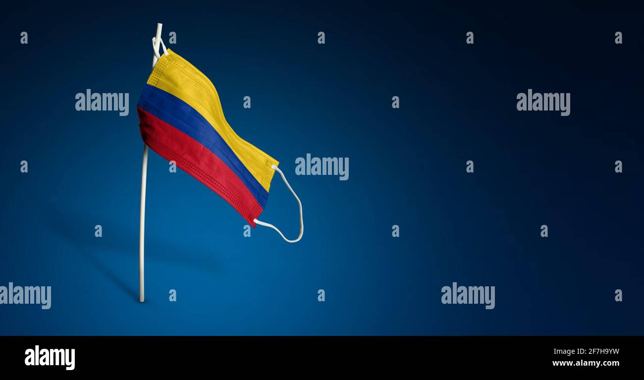 Maschera Colombia su sfondo blu scuro. Bandiera ondulata della Colombia dipinta su maschera medica sul palo. Flag di attacco del virus. Concetto della bandiera della lotta Foto Stock