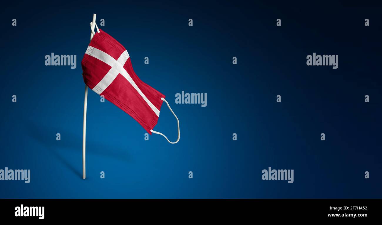 Maschera Danimarca su sfondo blu scuro. Bandiera ondulata della Danimarca dipinta su maschera medica sul palo. Flag di attacco del virus. Concetto del banner della Fight ag Foto Stock