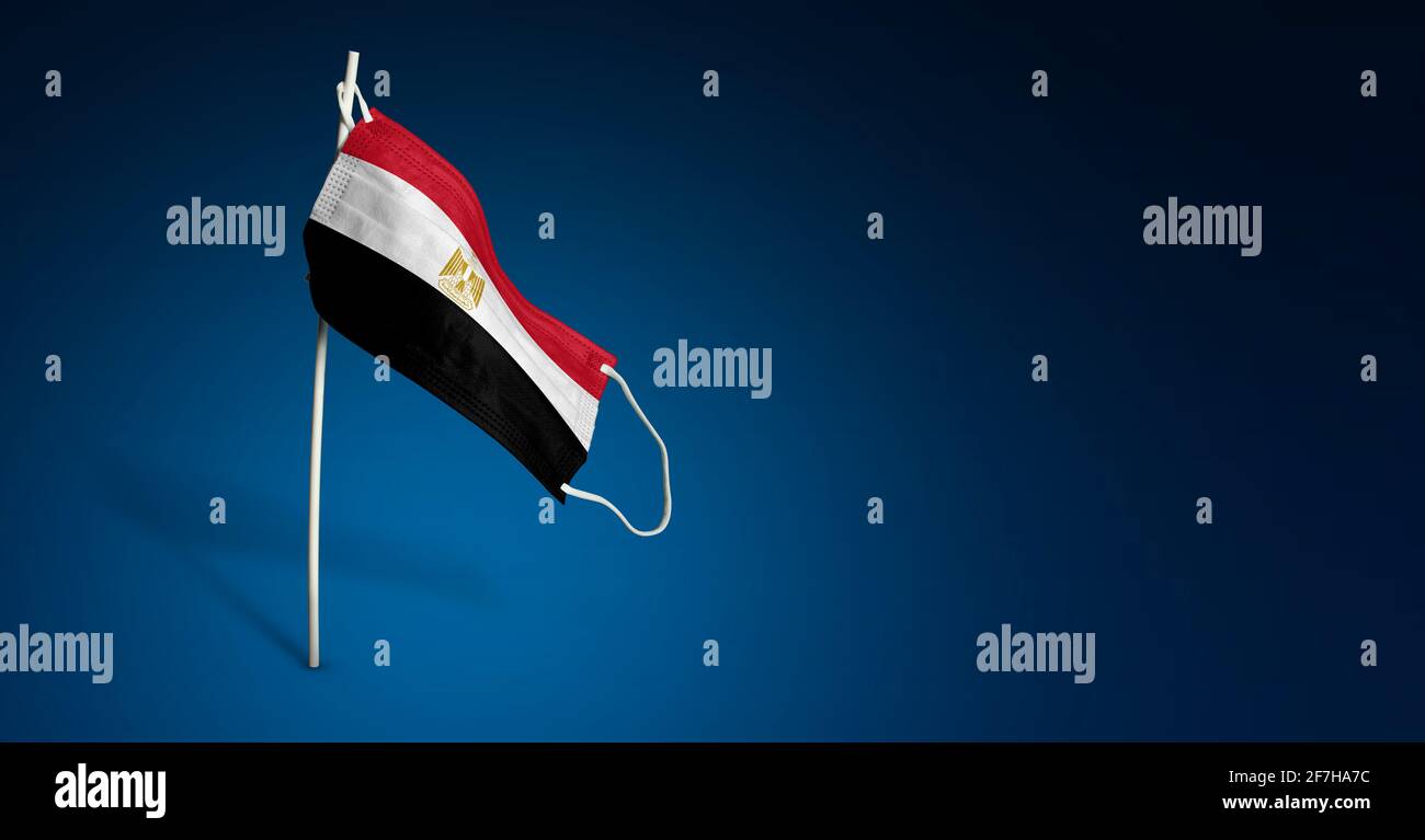 Maschera egiziana su sfondo blu scuro. Bandiera ondulata dell'Egitto dipinta su maschera medica sul palo. Flag di attacco del virus. Concetto della bandiera della lotta contro Foto Stock