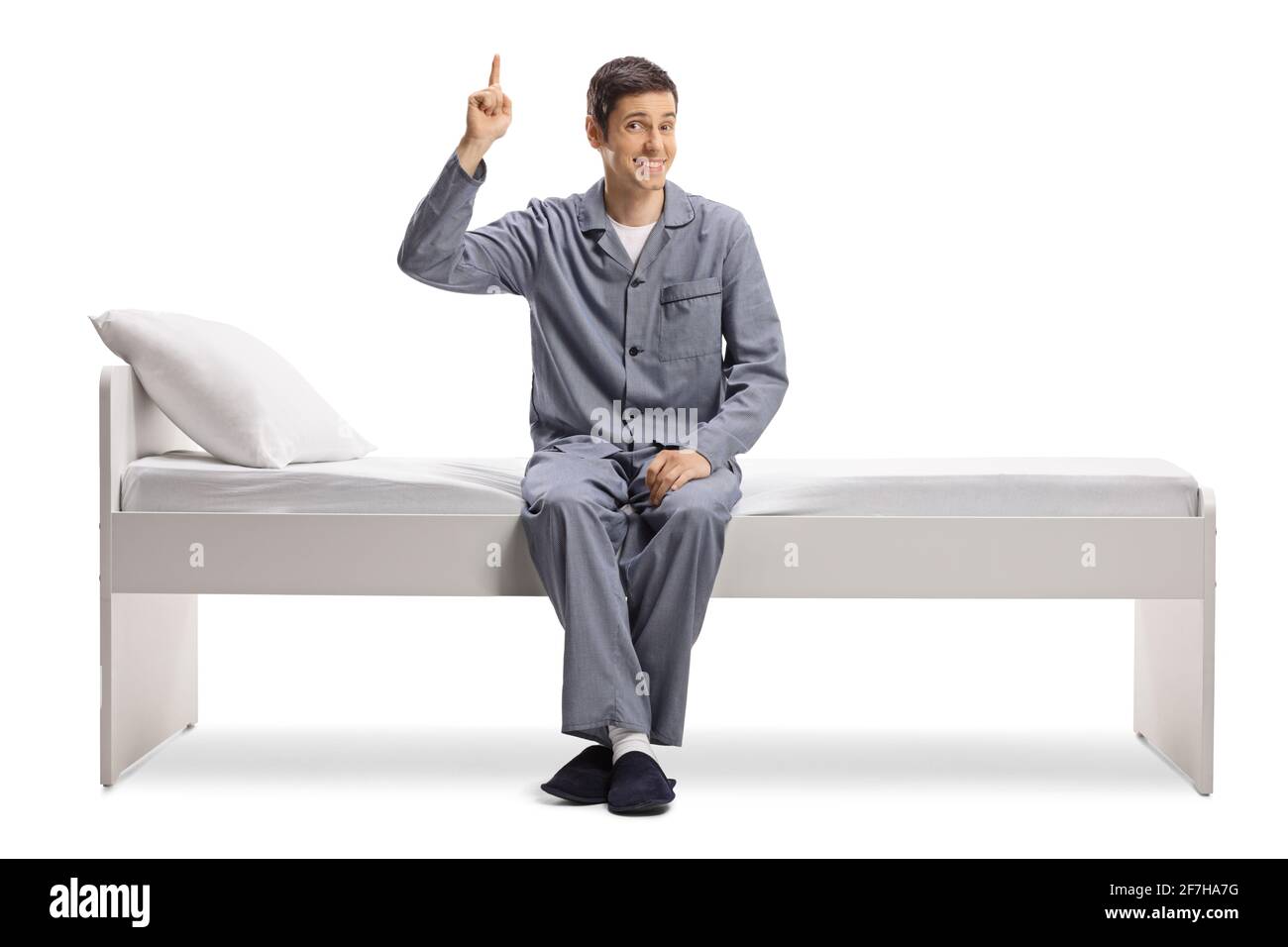 Sorridente giovane in pigiama seduto su un letto e. puntando verso l'alto isolato su sfondo bianco Foto Stock