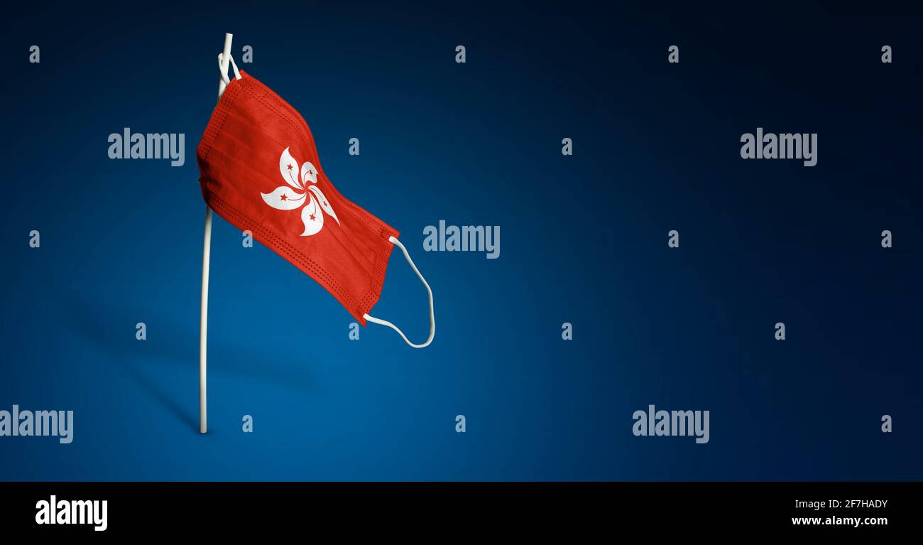 Maschera di Hong Kong su sfondo blu scuro. Bandiera ondulata di Hong Kong dipinta su maschera medica sul palo. Flag di attacco del virus. Concetto della bandiera della coscia Foto Stock