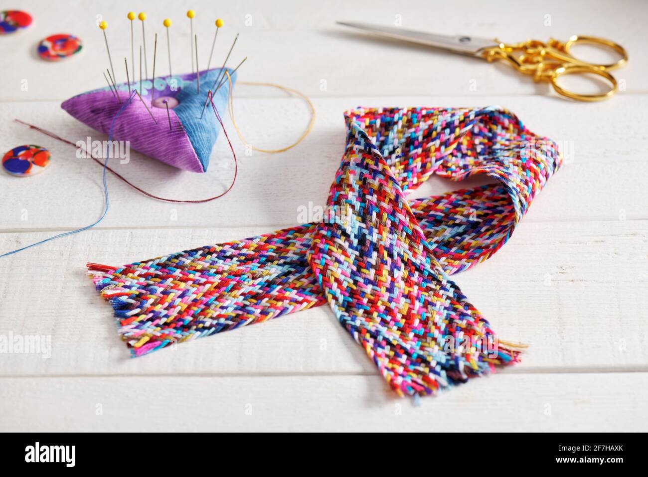 Una treccia di fili da cucire multicolore, pincushion, forbici, bottoni giacenti su una superficie bianca Foto Stock