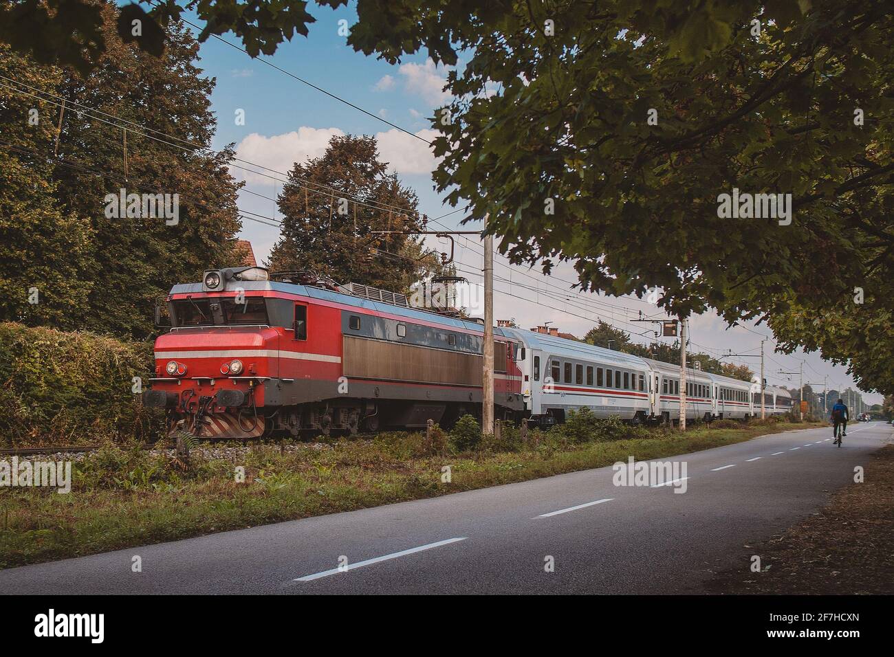 Moderno treno passeggeri con locomotiva rossa e carrozze bianche che corrono sui binari verso Lubiana. Treno veloce mattutino. Foto Stock