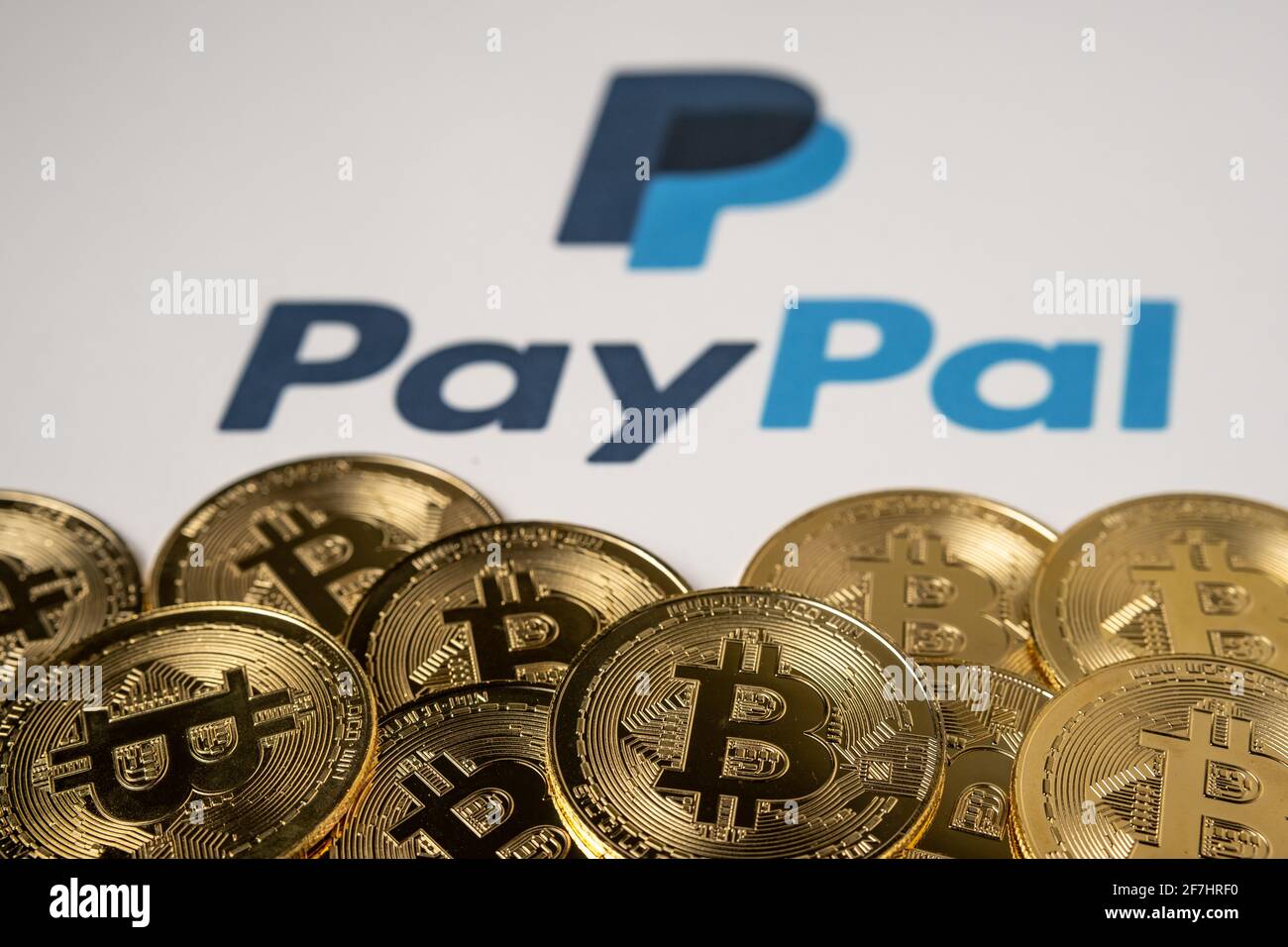 Monete di Bitcoin nella parte anteriore e logo PayPal sfocato sullo sfondo stampato della carta. Concetto. Messa a fuoco selettiva. Stafford, Regno Unito, 7 aprile 2021. Foto Stock