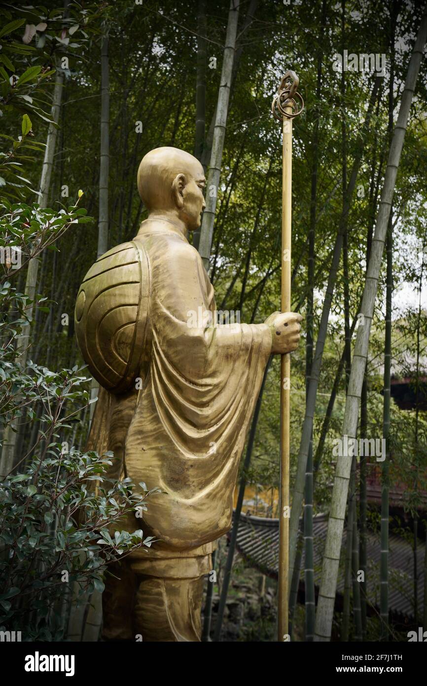 Una statua di bronzo di monaco che si trova nei boschi del Tempio Lingyin, circondato da un sacco di alberi di bambù. Foto Stock