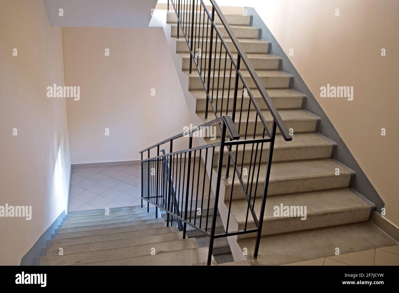 Scale all'ingresso di un edificio di appartamenti. Due rampe di scale con scalini in cemento e ringhiere in metallo nero lungo pareti beige, gli atterraggi a. Foto Stock