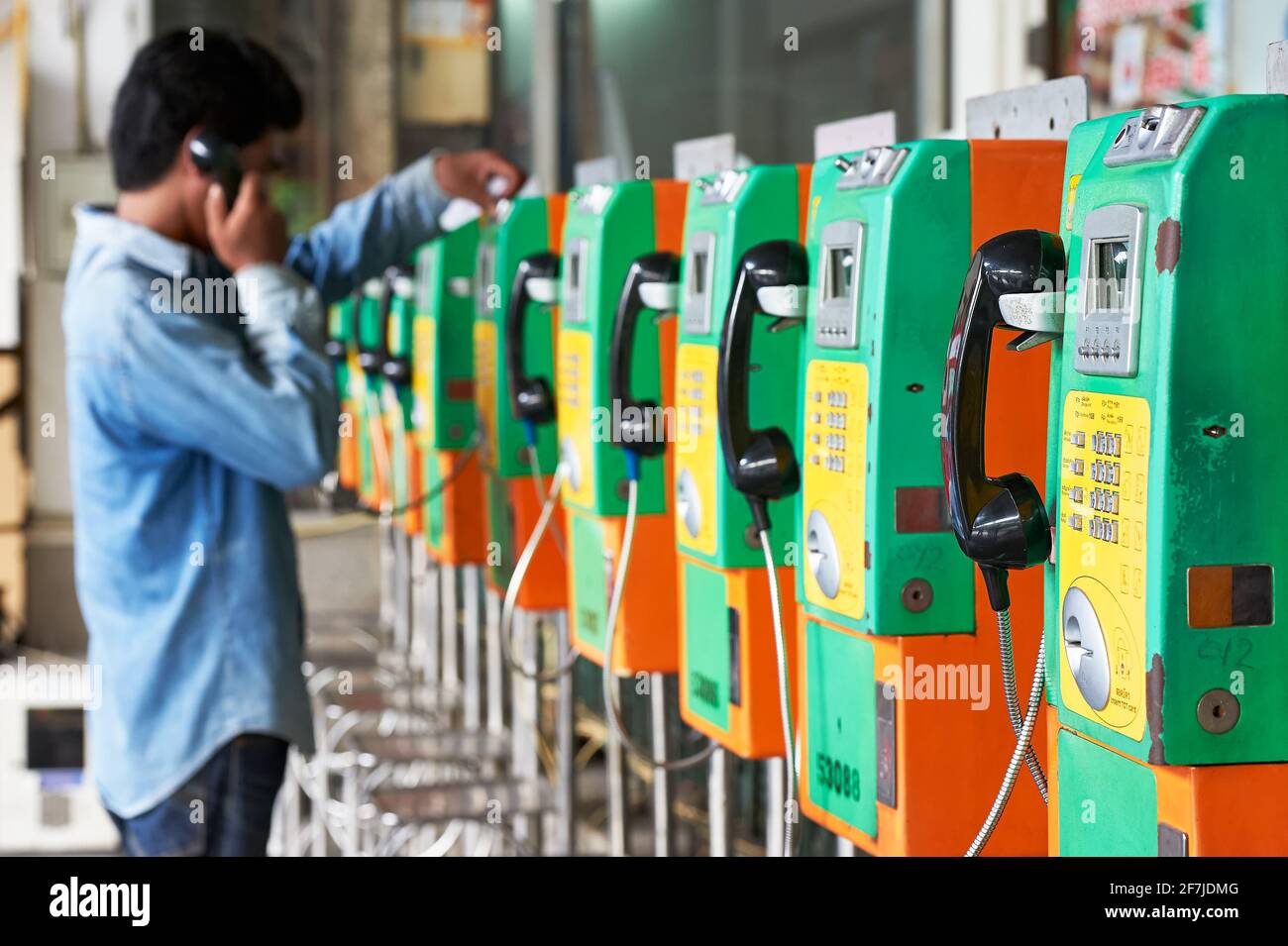 Una persona sta usando uno dei molti telefoni pubblici di colore verde e arancione tipici in una fila, collocati all'interno della stazione ferroviaria a Bangkok, Thailandia Foto Stock