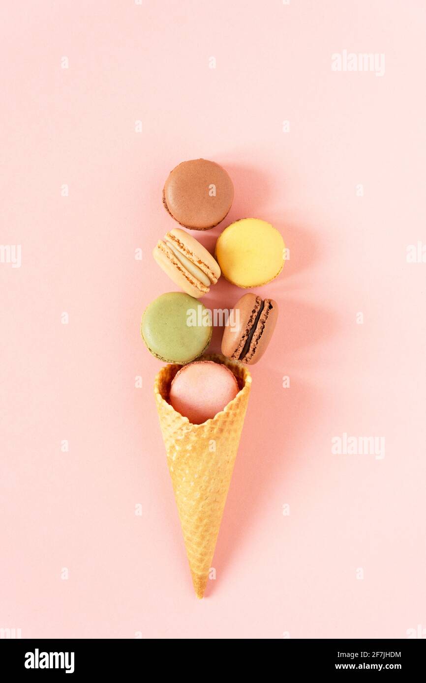 Varietà di macaron in un cono gelato waffle su sfondo rosa vista dall'alto. Composizione creativa di macaron di biscotti alla meringa francese. Foto Stock