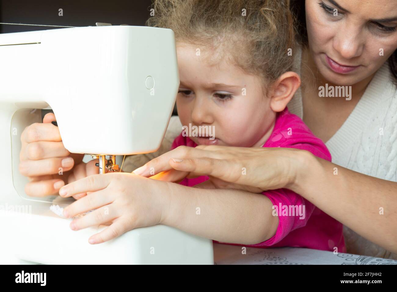 Bambina sta imparando da sua madre ad usare una macchina da cucire. Fuoco selettivo ragazza Foto Stock