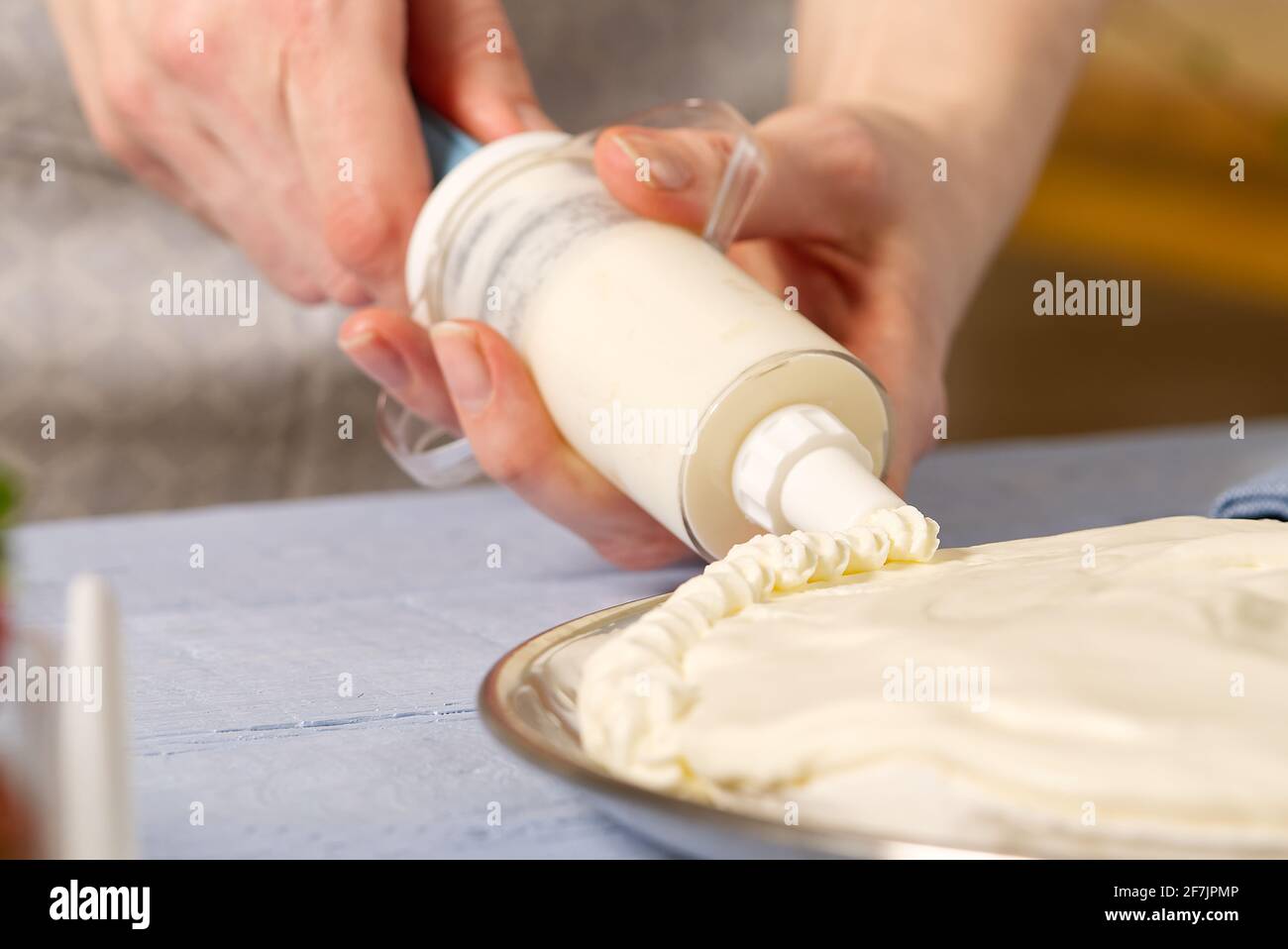 la panettiera donna strizza la panna montata. Torta di fragole fatta in casa con torta di meringa e crema con fragole. Foto Stock