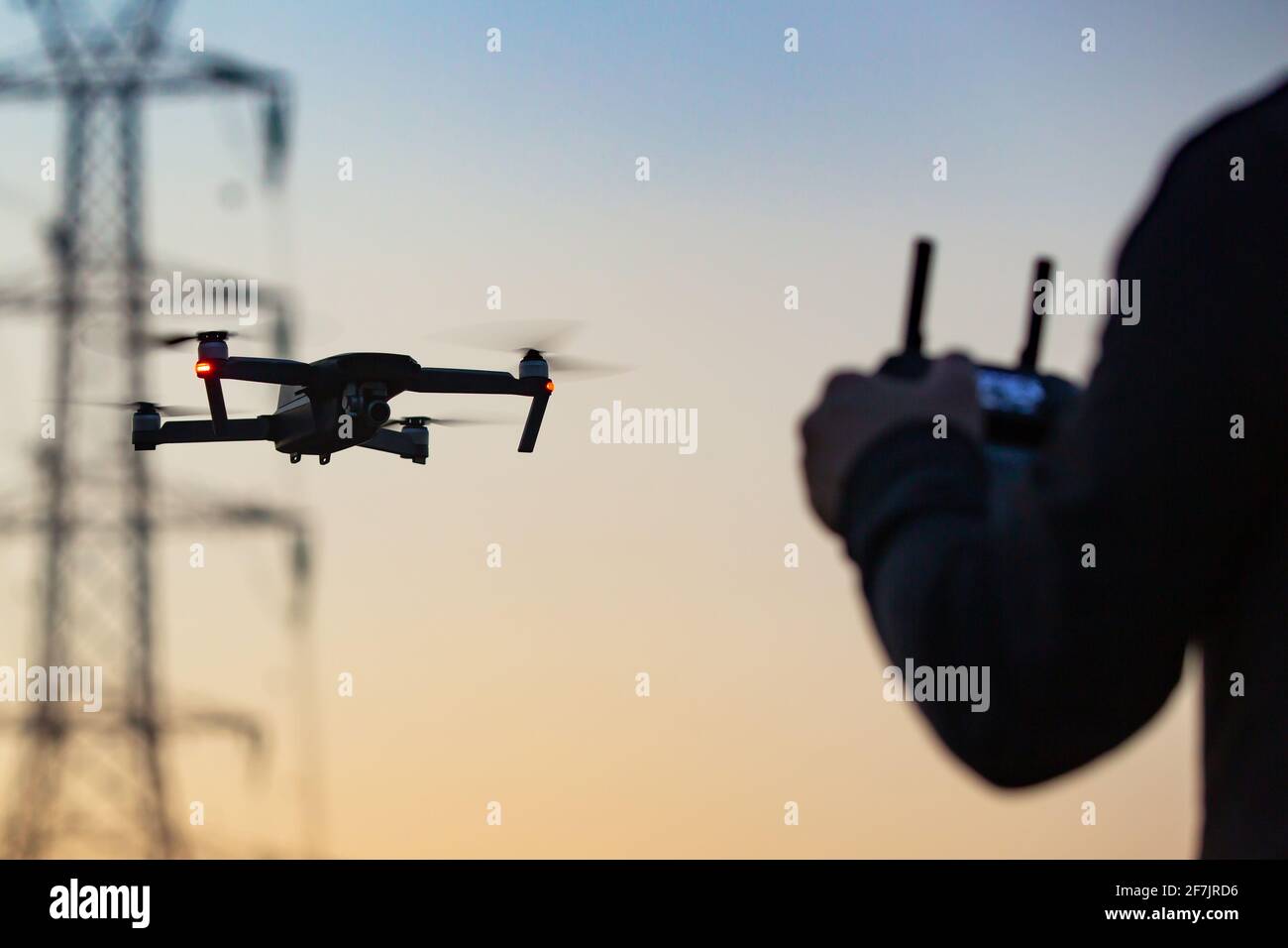 Un concetto di un uomo che vola su un drone che raccoglie dati a distanza da una centrale elettrica o per telecomunicazioni. Sicurezza dei droni, linee elettriche. Foto Stock