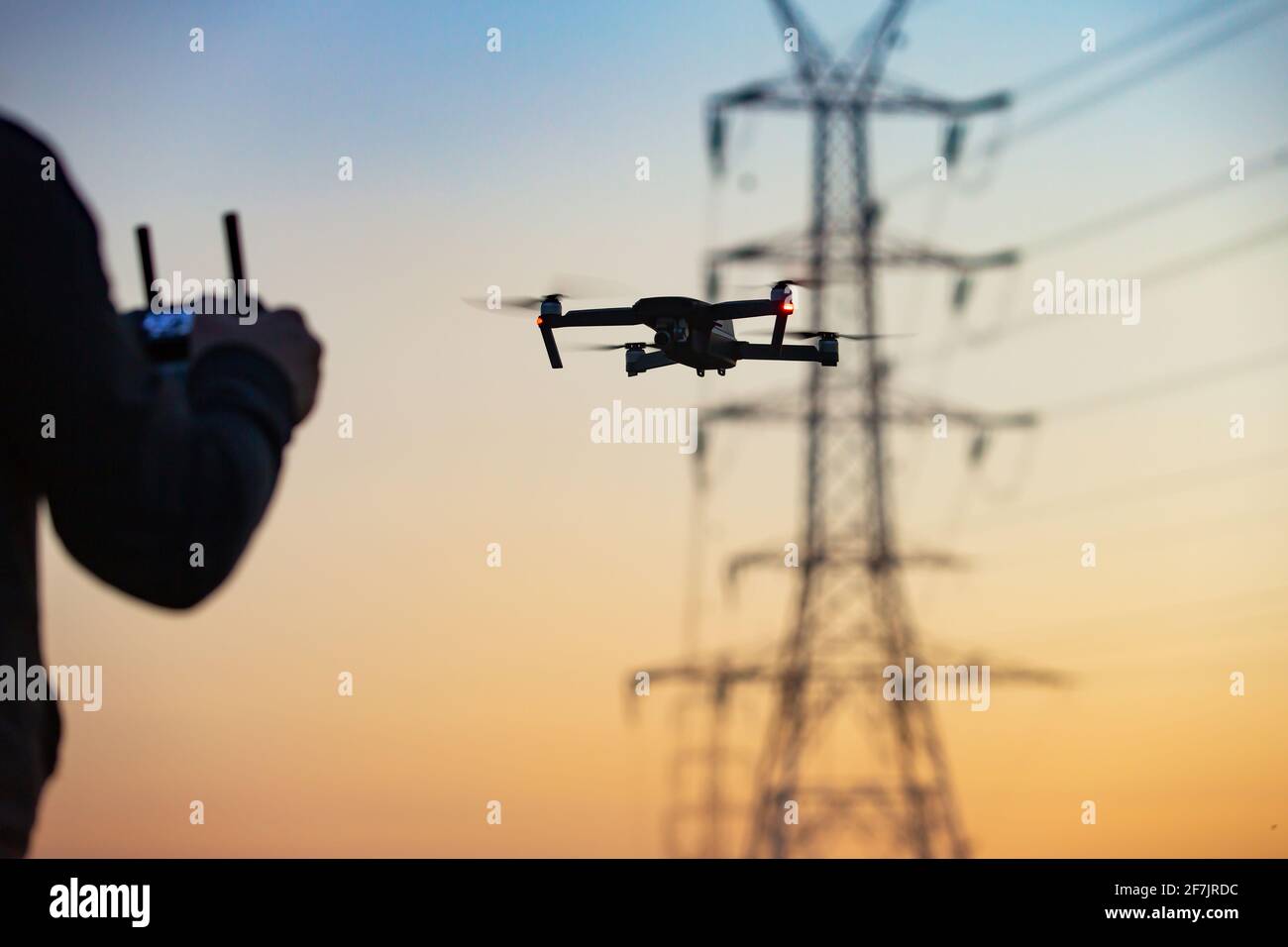 Un concetto di un uomo che vola su un drone che raccoglie dati a distanza da una centrale elettrica o per telecomunicazioni. Sicurezza dei droni, linee elettriche. Foto Stock