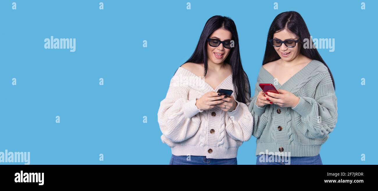 Banner, formato lungo su blu. Visualizzazione online di film delle gemelle femminili, sorelle che indossano occhiali 3D navigando sugli smartphone. Area Provino Foto Stock