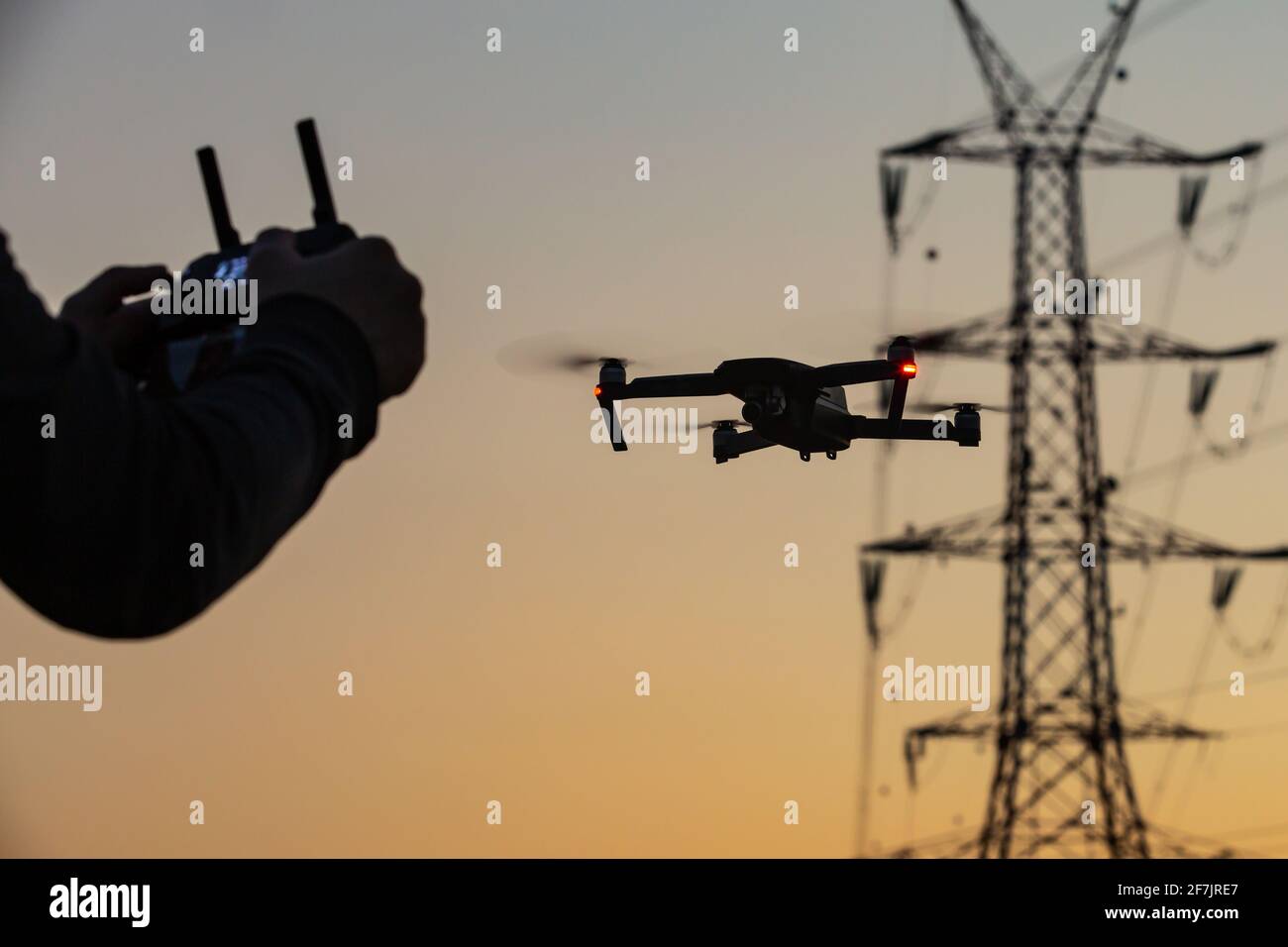 Un concetto di un uomo che vola su un drone che raccoglie dati a distanza da una centrale elettrica o per telecomunicazioni. Sicurezza dei droni, linee elettriche. Foto Stock