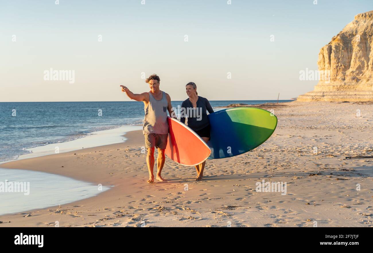 Coppia matura con tavole da surf sulla bellissima spiaggia godendo di paradiso e di uno stile di vita attivo. Bella forma uomo e donna surf e divertirsi. In trave Foto Stock