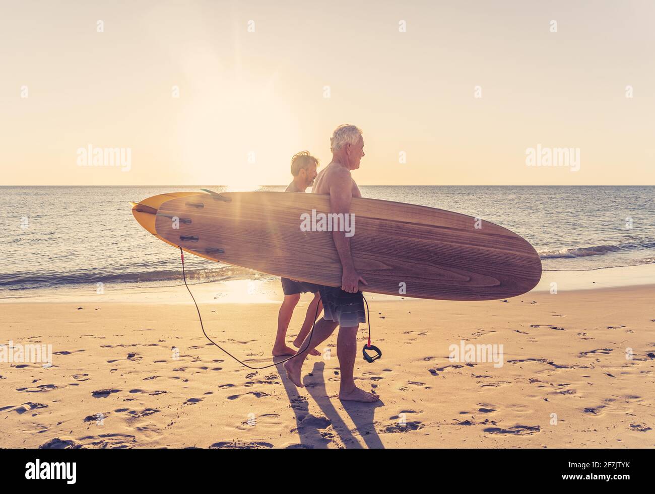 Due uomini maturi che camminano con tavole da surf sulla bellissima spiaggia godendo di paradiso e di vita di riposo. Amici adulti in forma attraente che si divertono Foto Stock