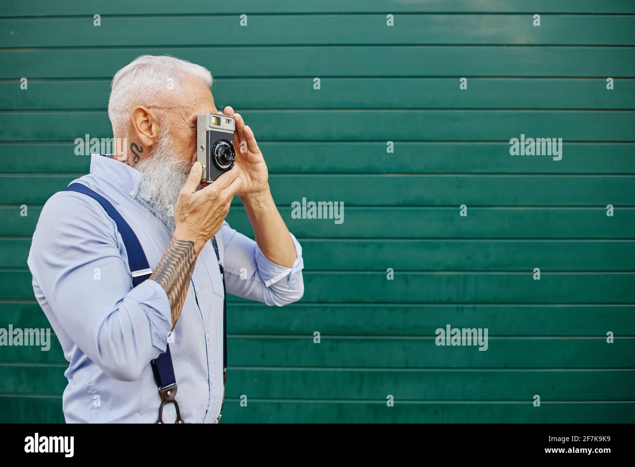 Happy Hipster uomo utilizzando la vecchia fotocamera vintage in piedi sulla parete rossa - matura fotografo elegante divertirsi in viaggio il mondo - gioioso stile di vita anziani Foto Stock