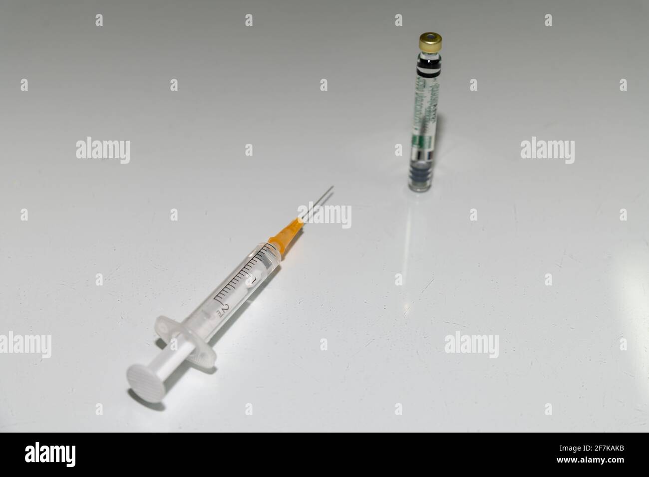 Siringa e ago con una dose di vaccino. Vaccino contro Corona, primo piano su una tavola bianca. Foto Stock
