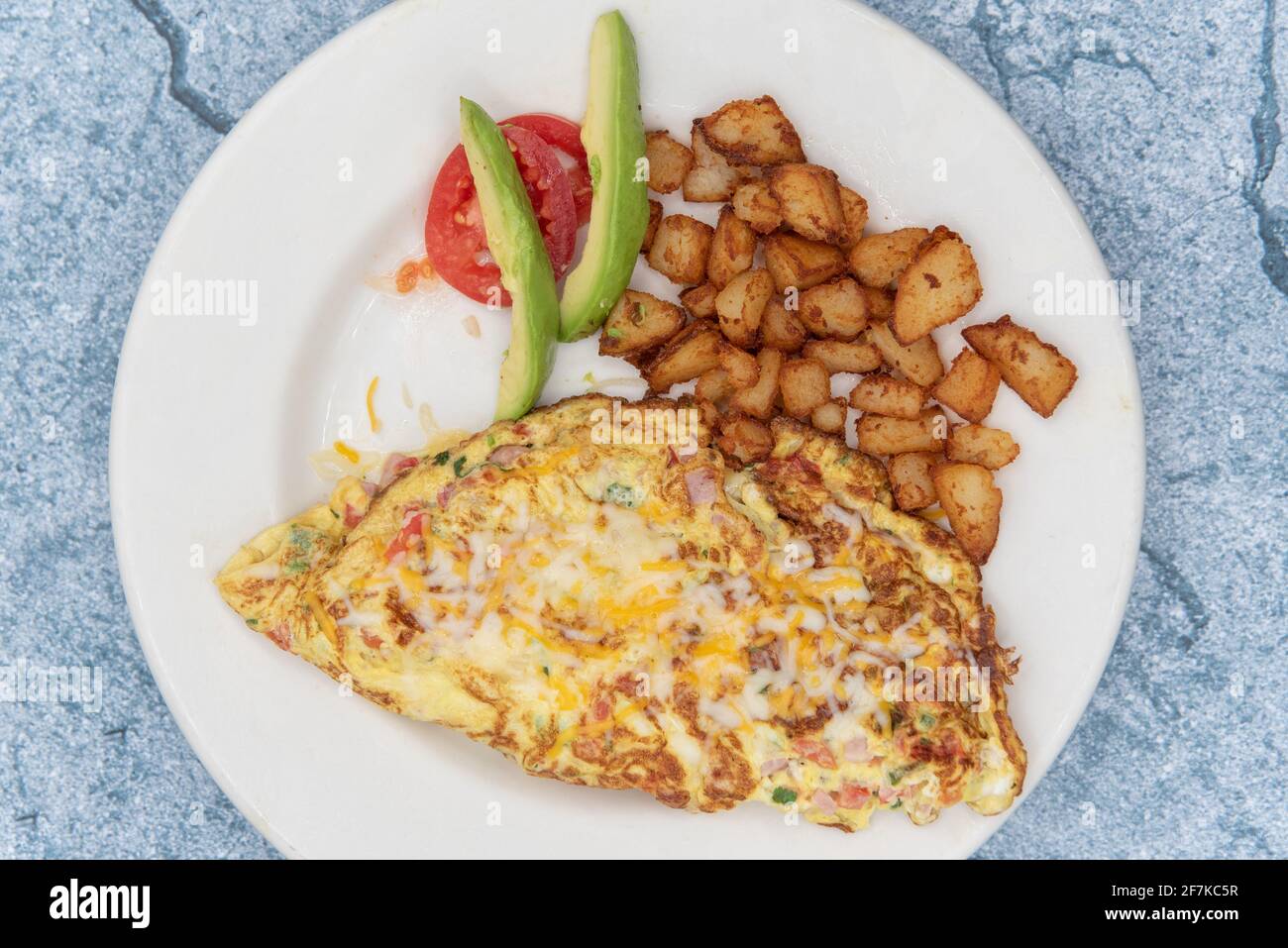 Vista dall'alto delle omelette cucinate al perfetto livello di frigidità ripiegate e servite con patate a cubetti e avocado a fette. Foto Stock