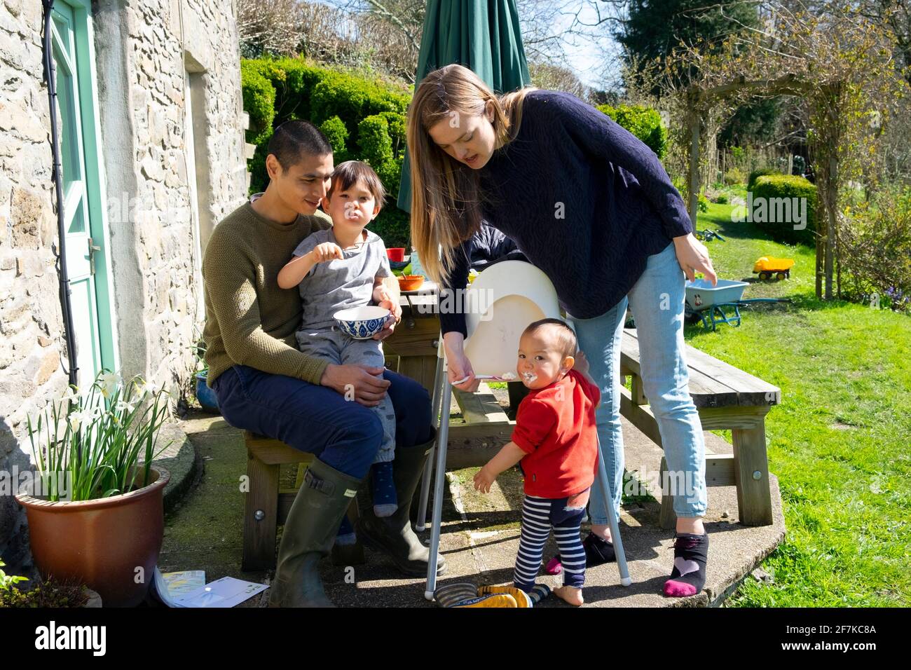 Genitori madre padre giovane razza mista famiglia seduta fuori alimentazione Bambini nel soleggiato week-end pasquale in un giardino in Occidente GALLES REGNO UNITO KATHY DEWITT Foto Stock