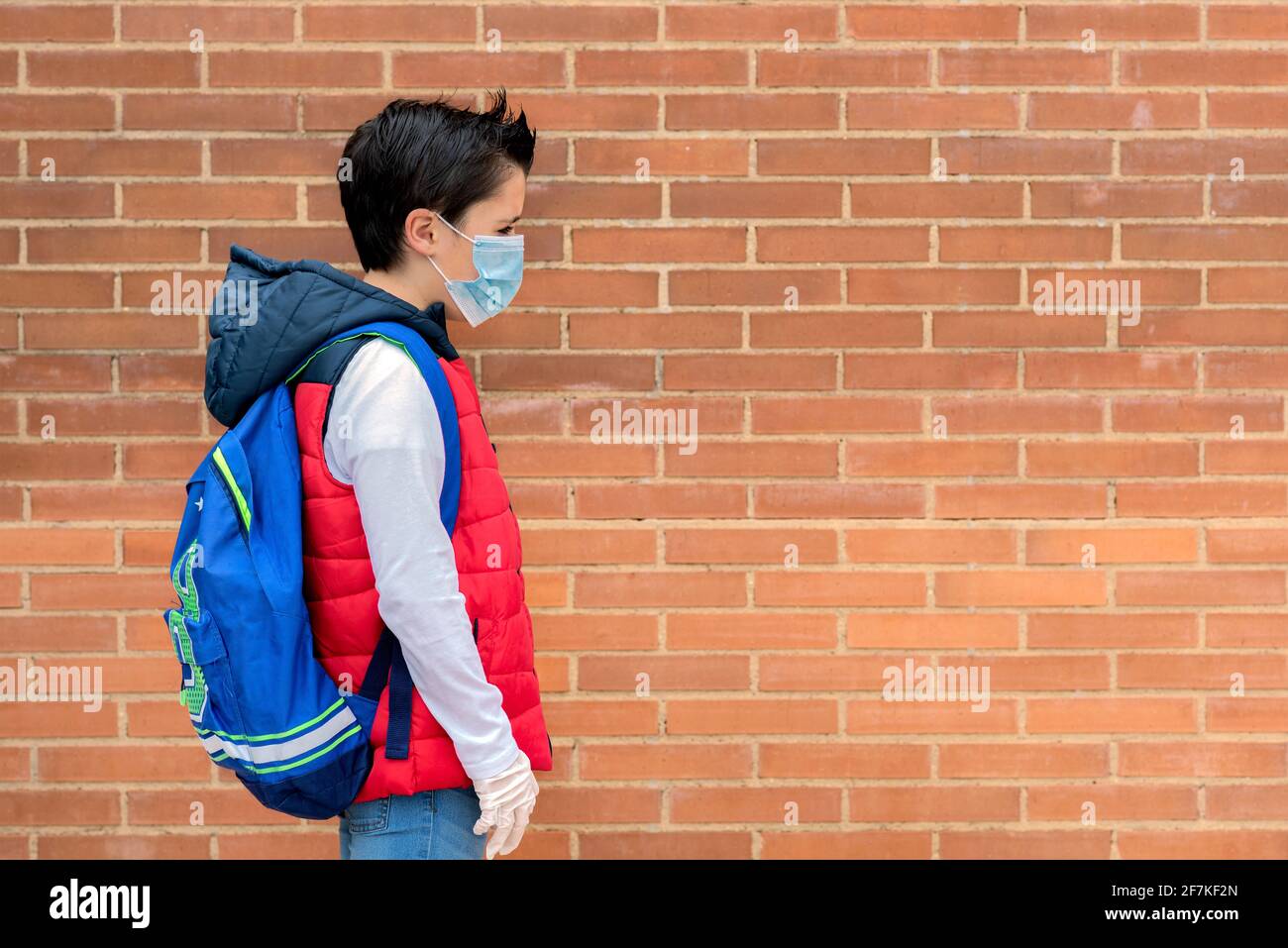 bambino triste e penoso con maschera chirurgica protettiva e zaino andare a scuola all'aperto Foto Stock