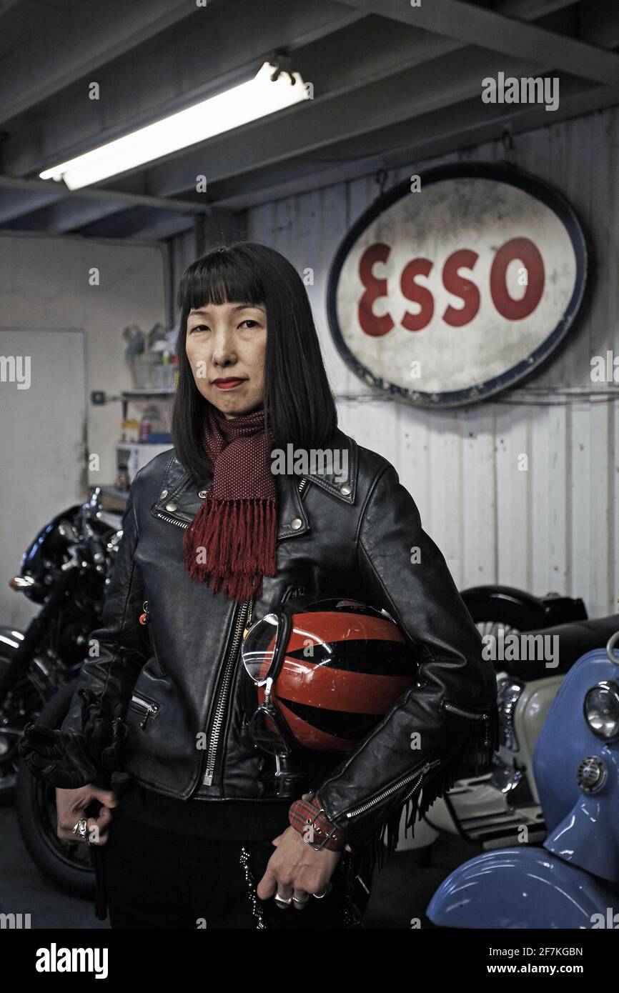 Femmina Rocker con giacca in pelle in piedi in officina con segno esso in background a Londra, Regno Unito Foto Stock