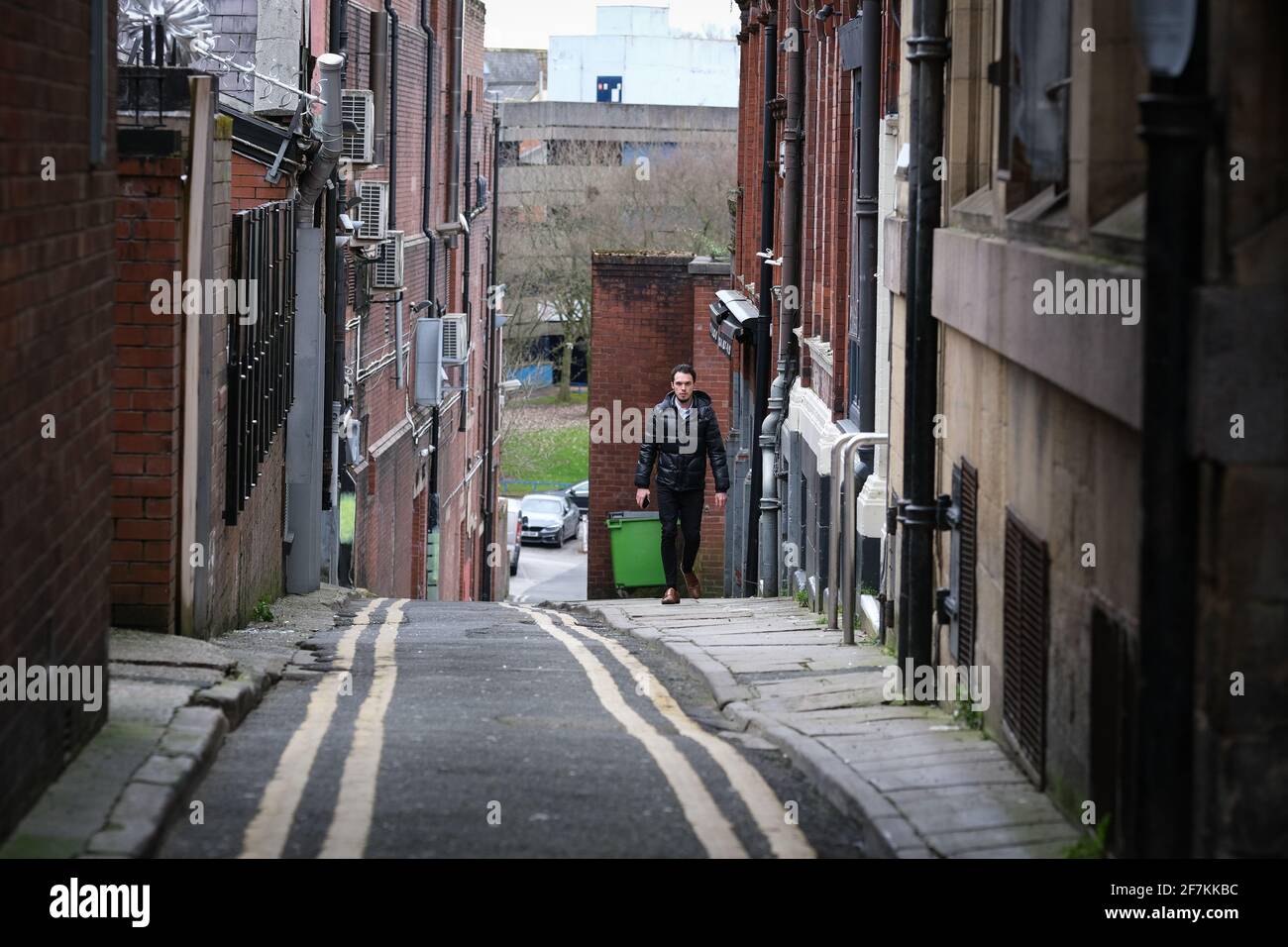 Uomo che cammina lungo la stretta strada laterale a Preston, Lancashire, Regno Unito. Foto Stock